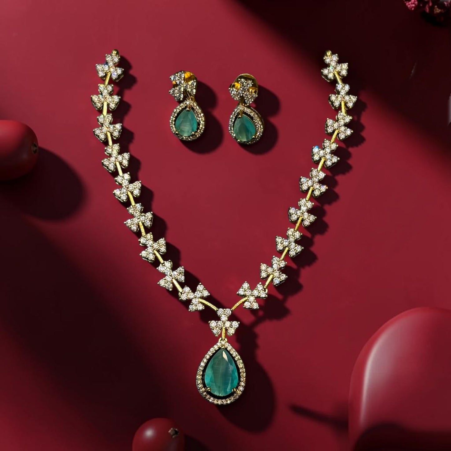 My Store teardrop pendant necklace and earring set with green stones and sparkling floral motifs on a red background