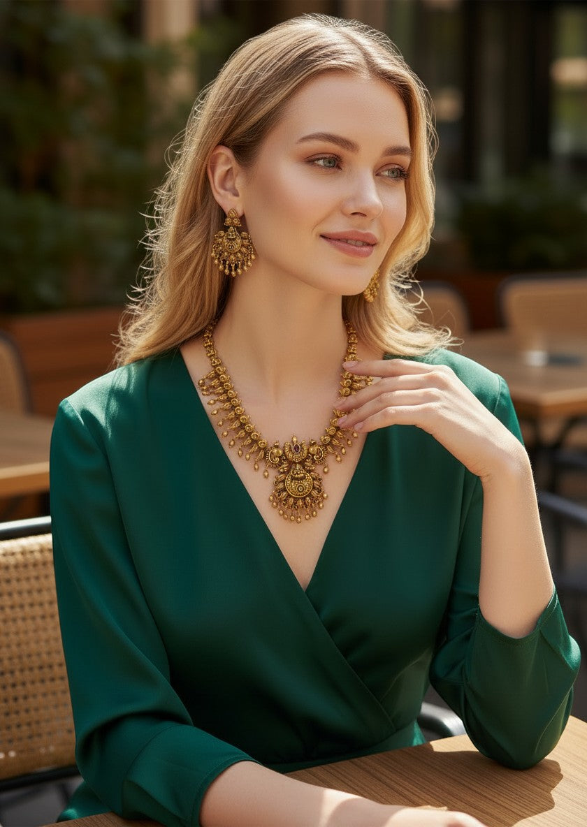My Store antique gold-toned necklace and earring set with temple motifs and ruby stones worn by a woman in a green dress.
