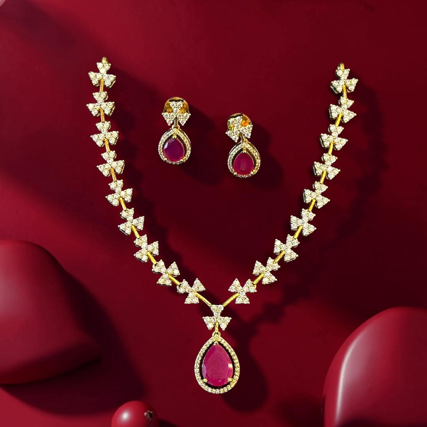 My Store gold teardrop necklace and earring set with ruby-red stones and sparkling floral motifs on a red background