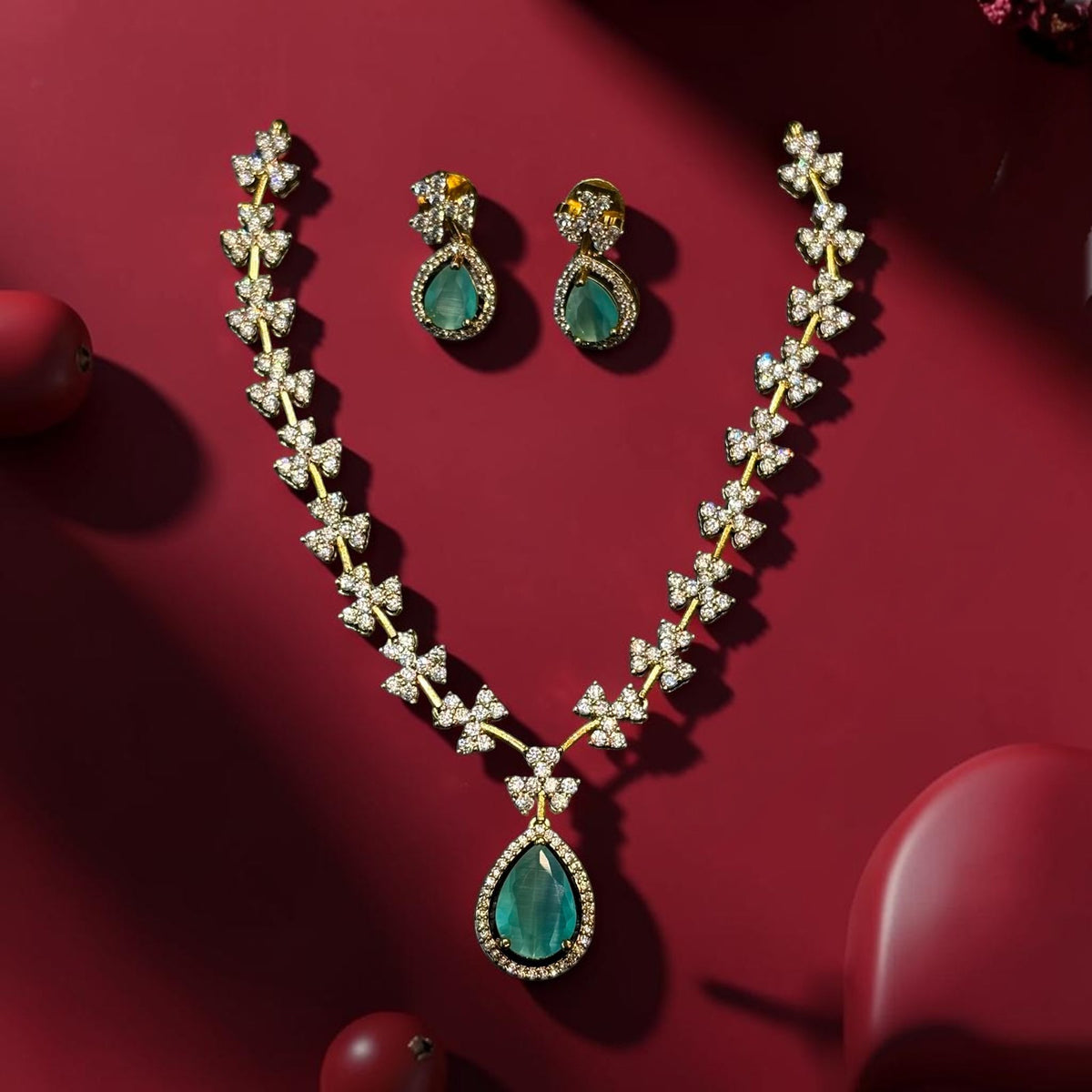 My Store teardrop pendant necklace and earring set with green stones and sparkling floral motifs on a red background